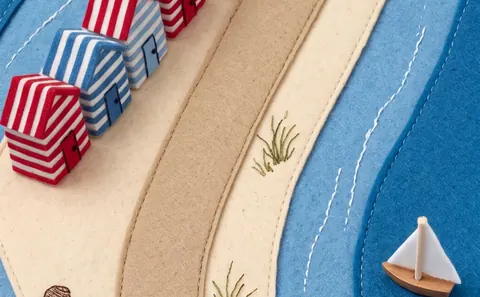 Tide: striped beach huts on a sandy path by a felt sea.